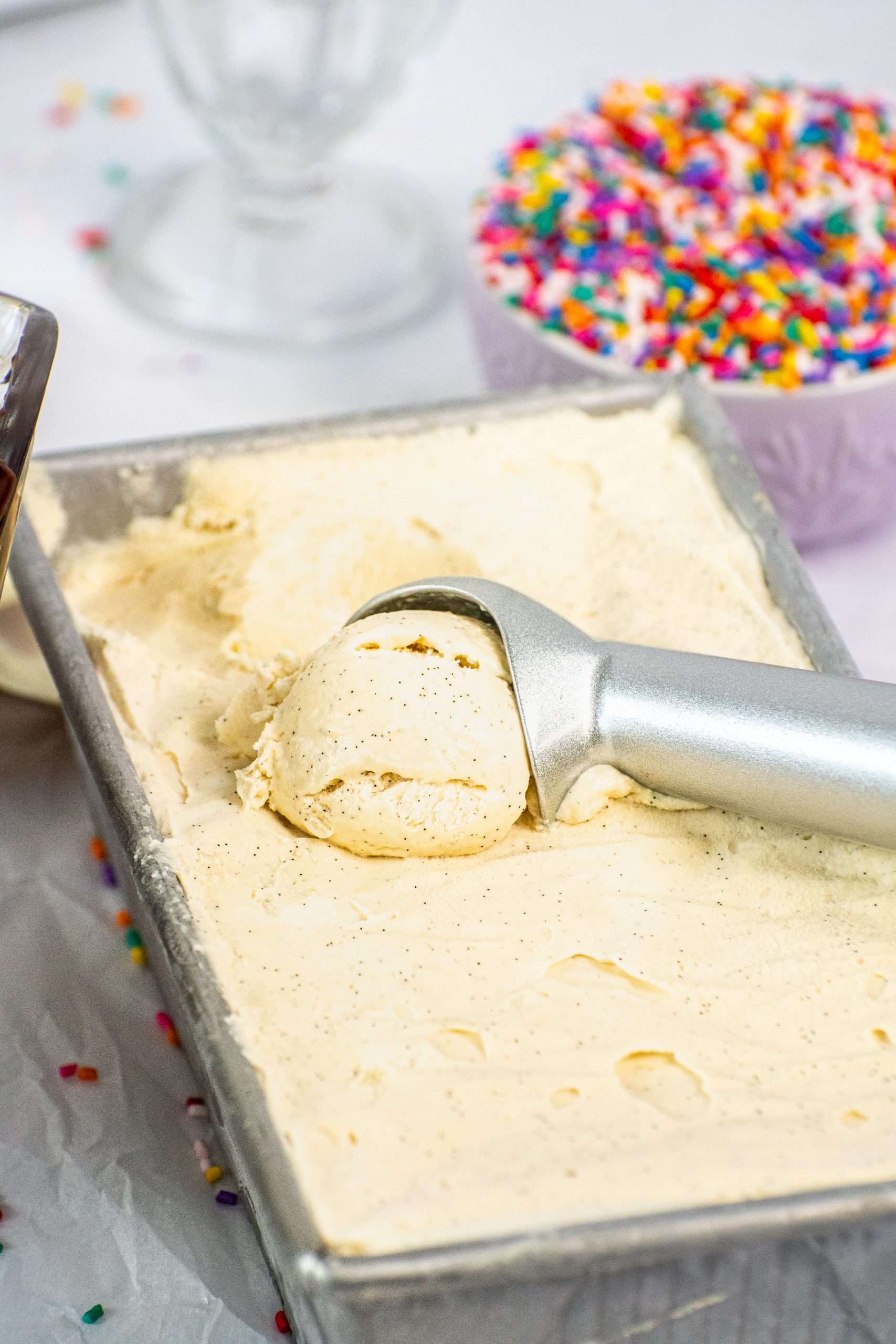 Close-up of a scoop of no churn vanilla ice cream with visible vanilla bean specks in a metal loaf pan.