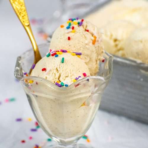 Two scoops of no churn vanilla ice cream with rainbow sprinkles in a glass dessert dish and a gold spoon.