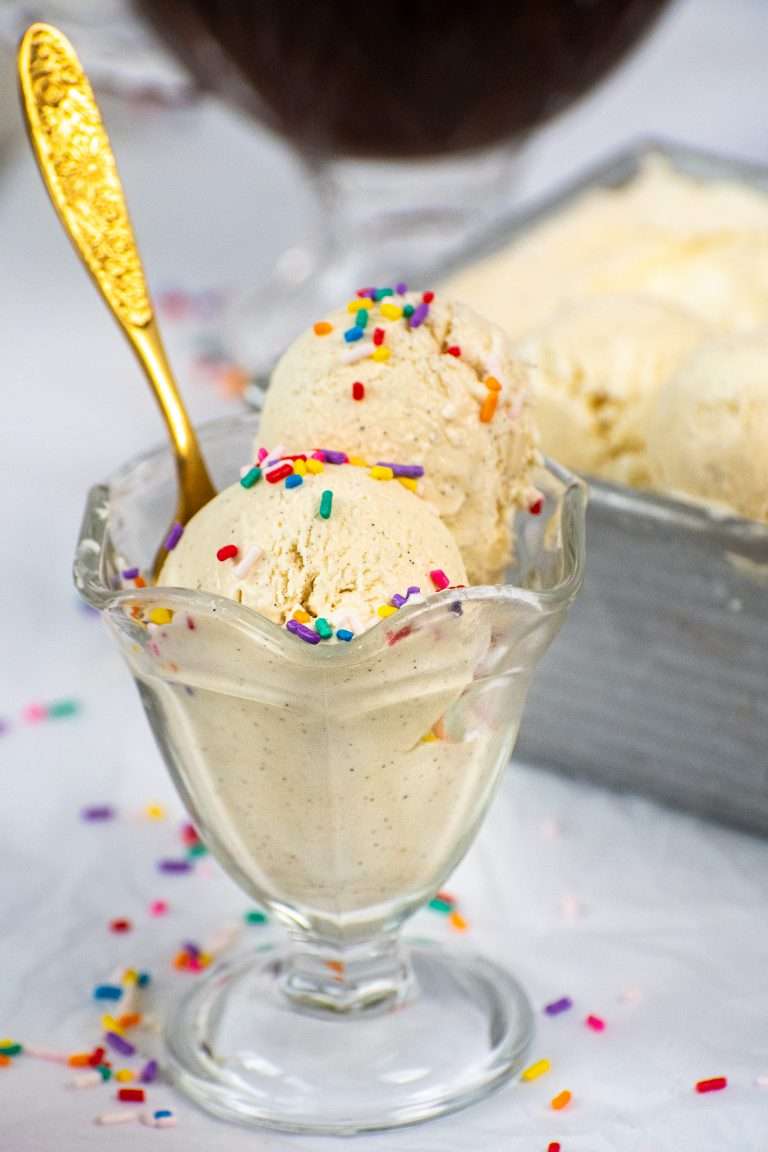 Two scoops of no churn vanilla ice cream with rainbow sprinkles in a glass dessert dish and a gold spoon.