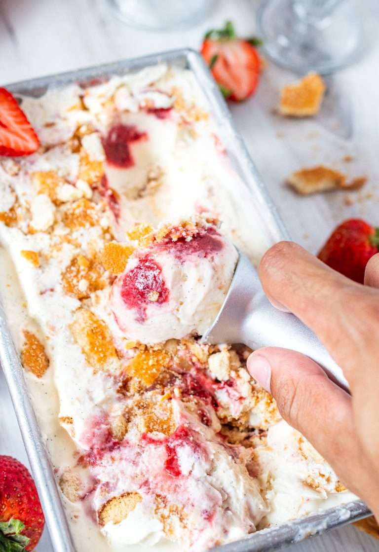 Scooping strawberry shortcake ice cream with swirls of strawberry sauce and crushed cookie topping from a metal loaf pan