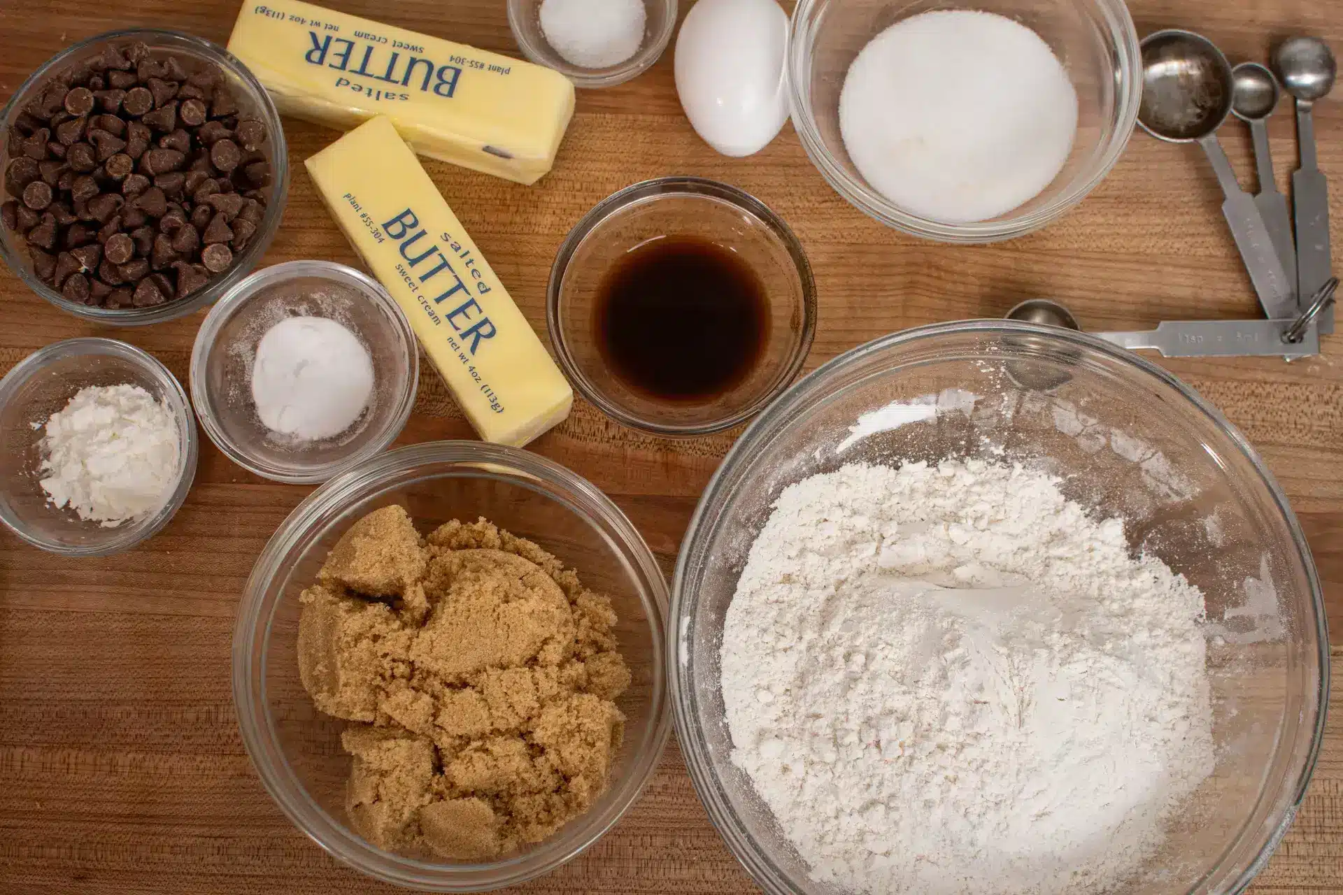 Ingredients for chocolate chip cookies, including butter, flour, sugar, brown sugar, vanilla, chocolate chips, and eggs.
