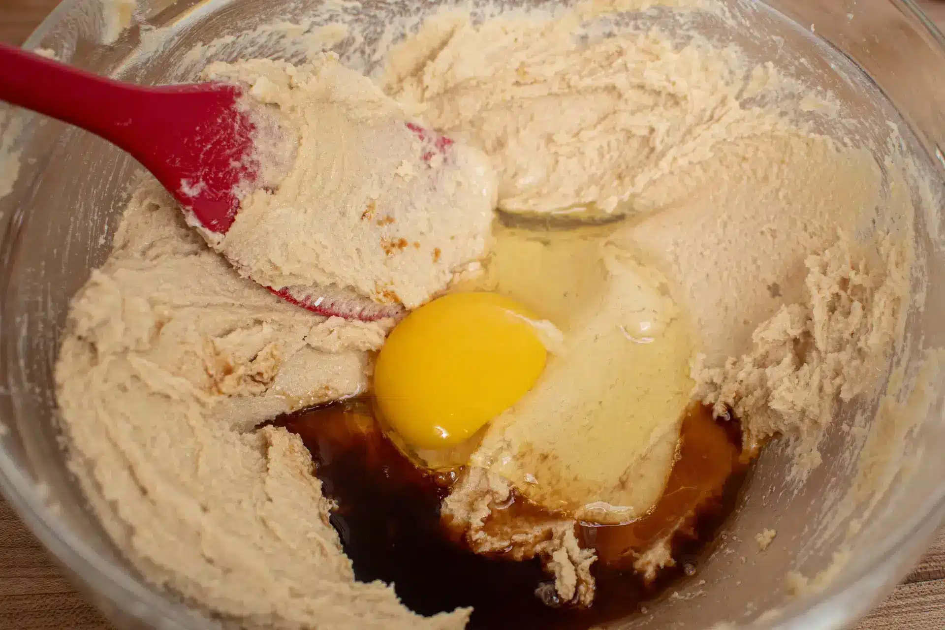 Egg and vanilla added to cookie dough in a mixing bowl.