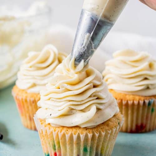 Piping whipped vanilla frosting onto funfetti cupcakes using a clear piping bag with a star tip,