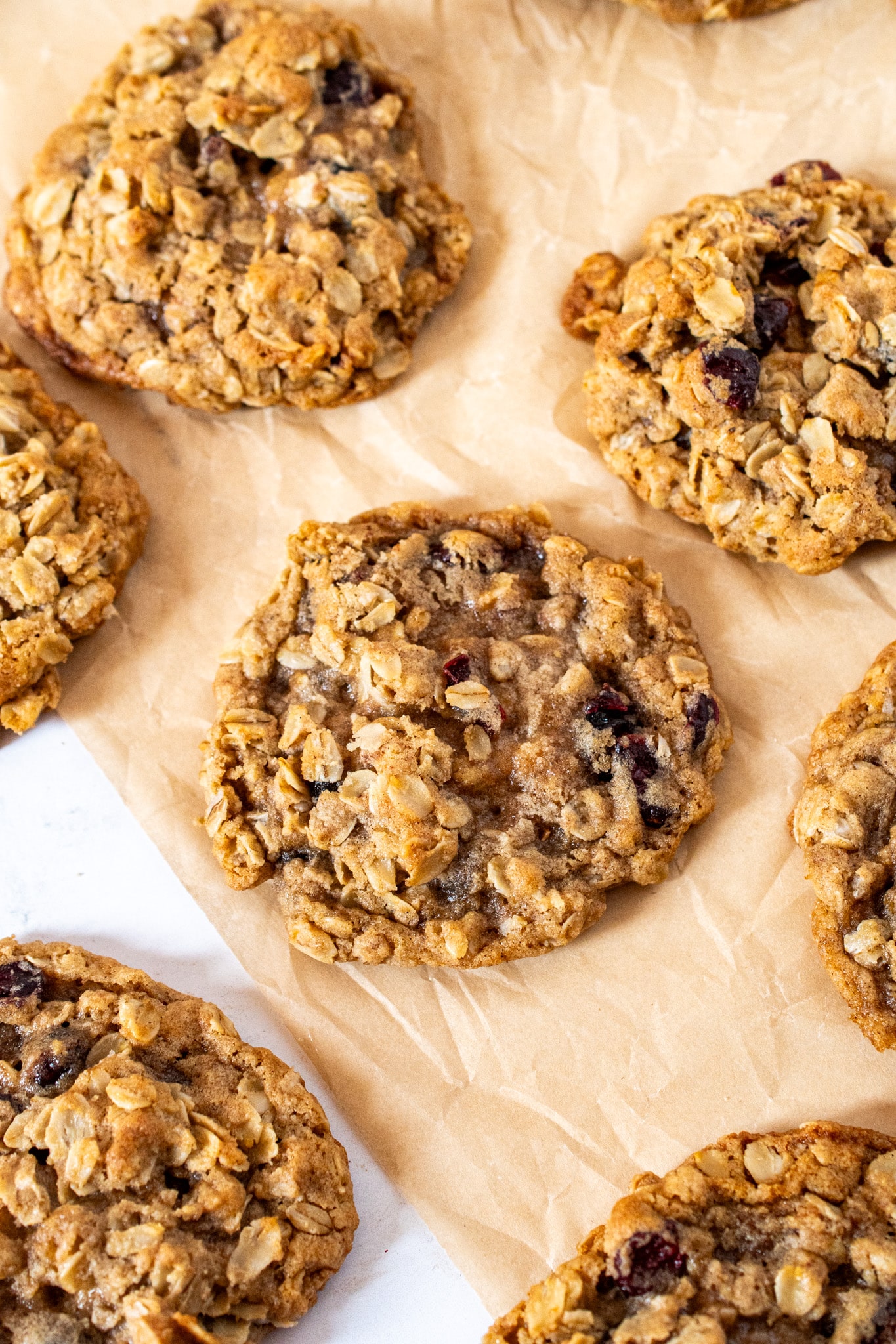 Soft and chewy oatmeal cranberry cookies on parchment paper with golden brown edges and visible oats and cranberries.
