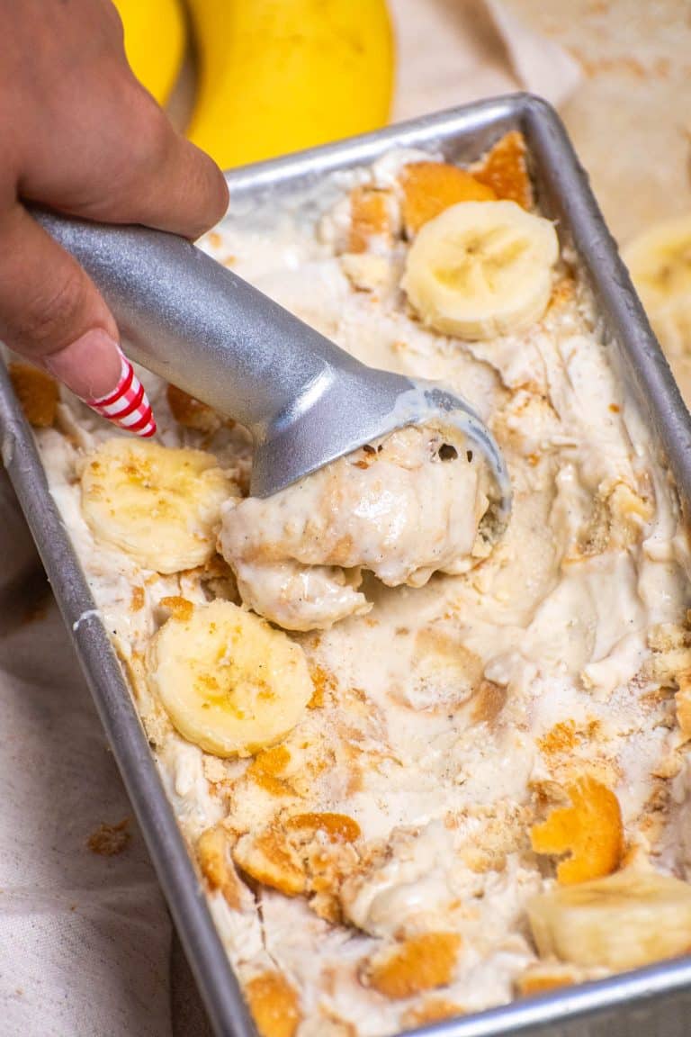 Scooping banana pudding ice cream with banana slices and crushed vanilla wafers in a loaf pan