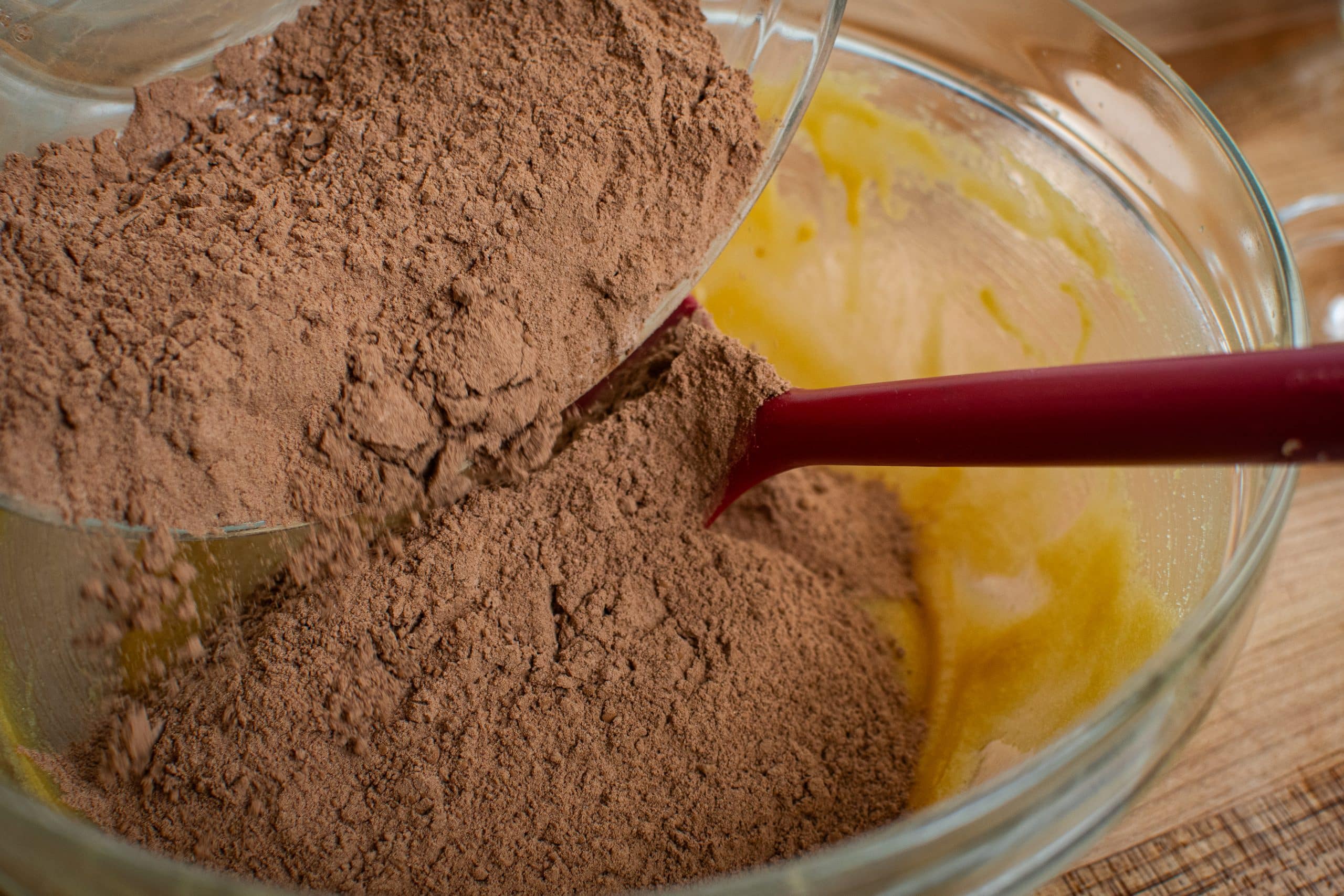Pouring dry ingredients into a mixing bowl with melted butter and sugar.