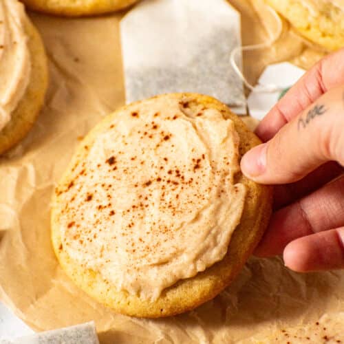 Hand sprinkling cinnamon on chai sugar cookie with eggnog icing