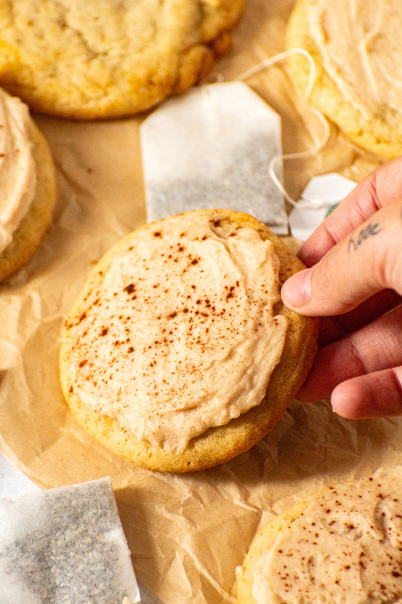 Hand sprinkling cinnamon on chai sugar cookie with eggnog icing
