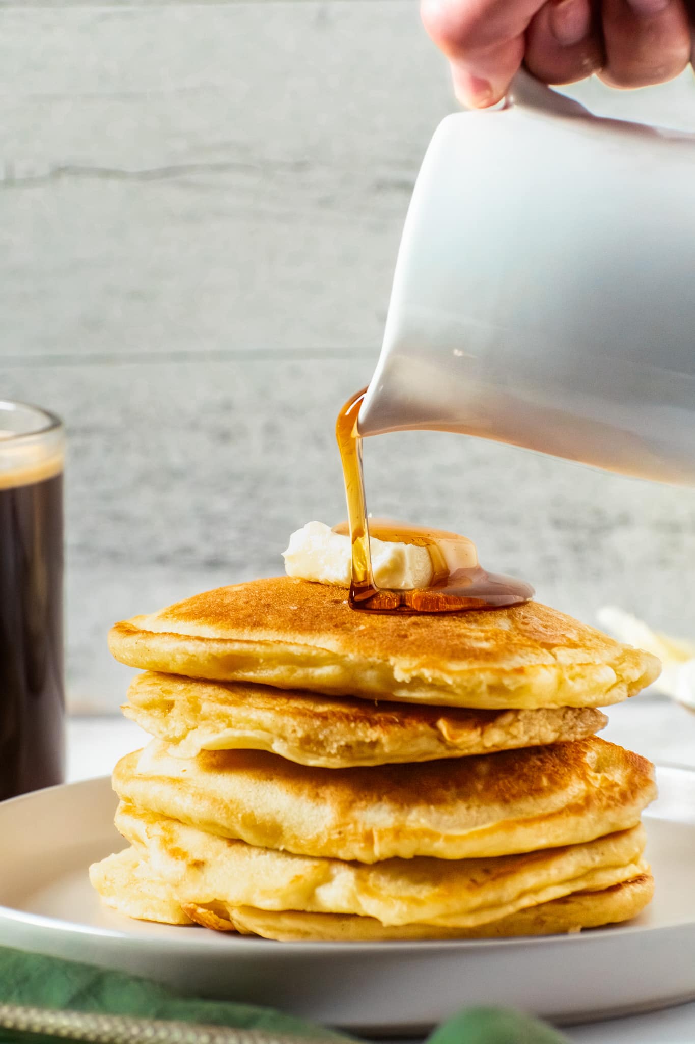 Maple syrup being poured over crispy edge buttermilk pancakes with butter on top