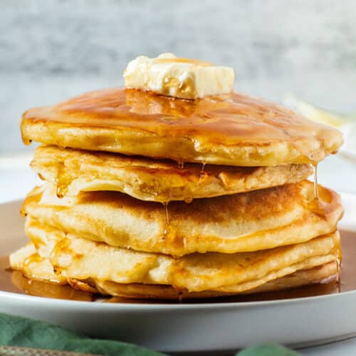 Crispy edge buttermilk pancakes stacked with melted butter and maple syrup, served warm