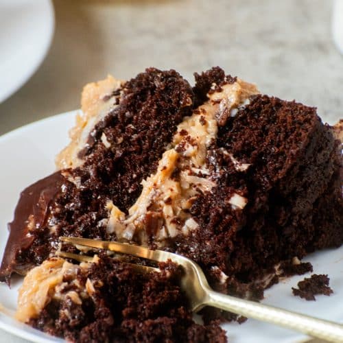 Moist slice of homemade German chocolate cake with coconut pecan filling and chocolate ganache on a white plate