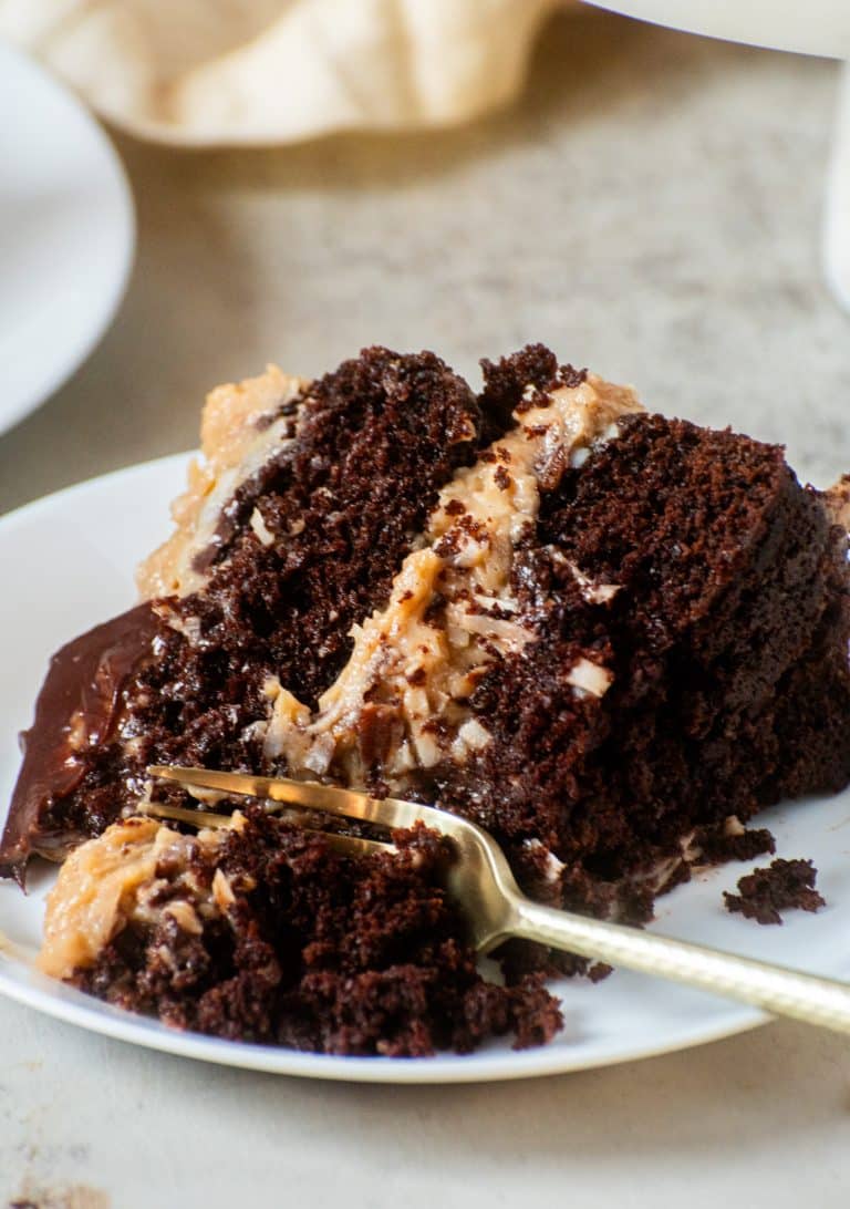 Moist slice of homemade German chocolate cake with coconut pecan filling and chocolate ganache on a white plate