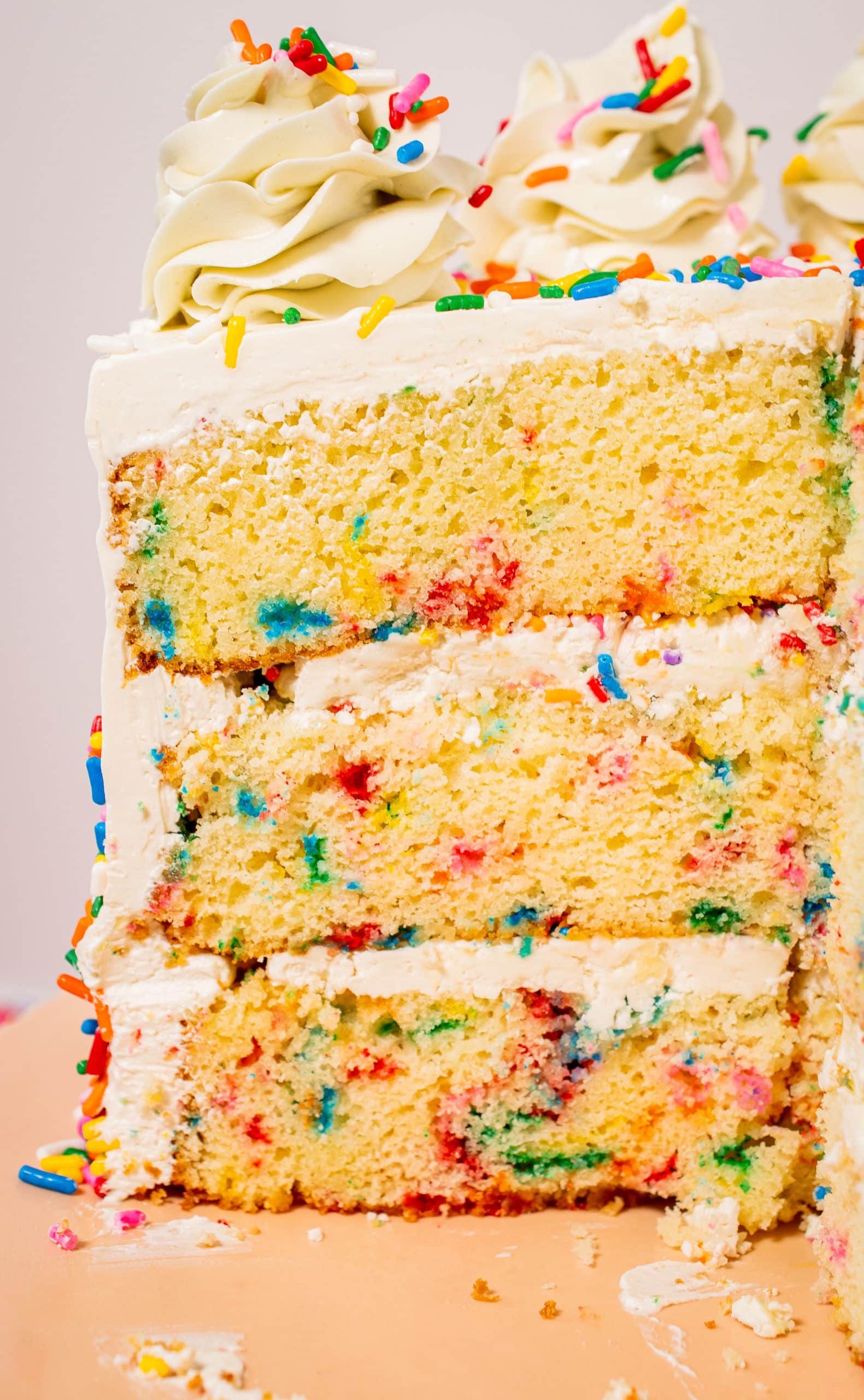 Close-up view of three-layer Funfetti cake with vanilla buttercream frosting and colorful sprinkles.