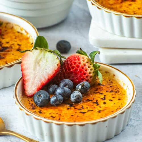 Vanilla bean crème brûlée with a crisp caramelized sugar top, garnished with fresh strawberries and blueberries