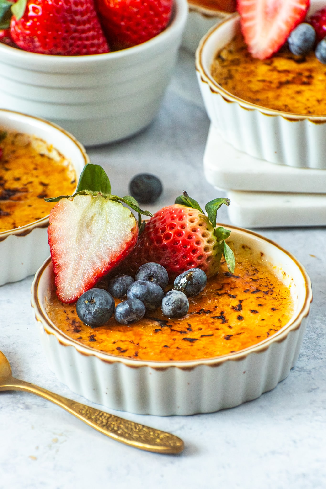 Vanilla bean crème brûlée with a crisp caramelized sugar top, garnished with fresh strawberries and blueberries