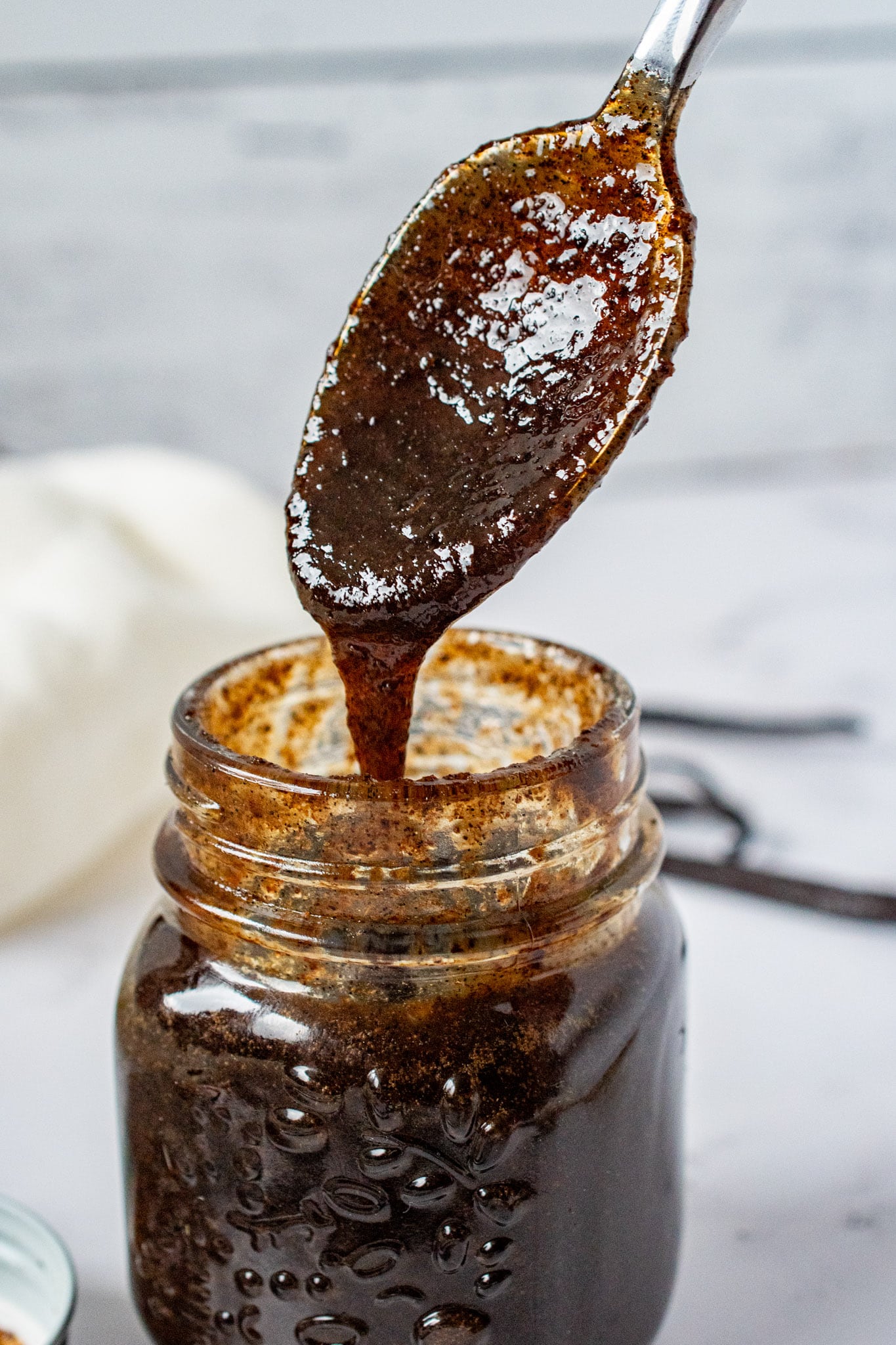 Thick vanilla bean paste dripping from a spoon into a glass jar.