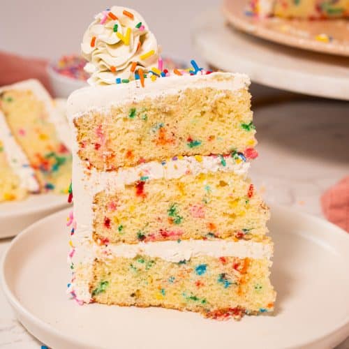 Three-layer Funfetti cake with vanilla buttercream frosting and colorful sprinkles, displayed on a white plate.
