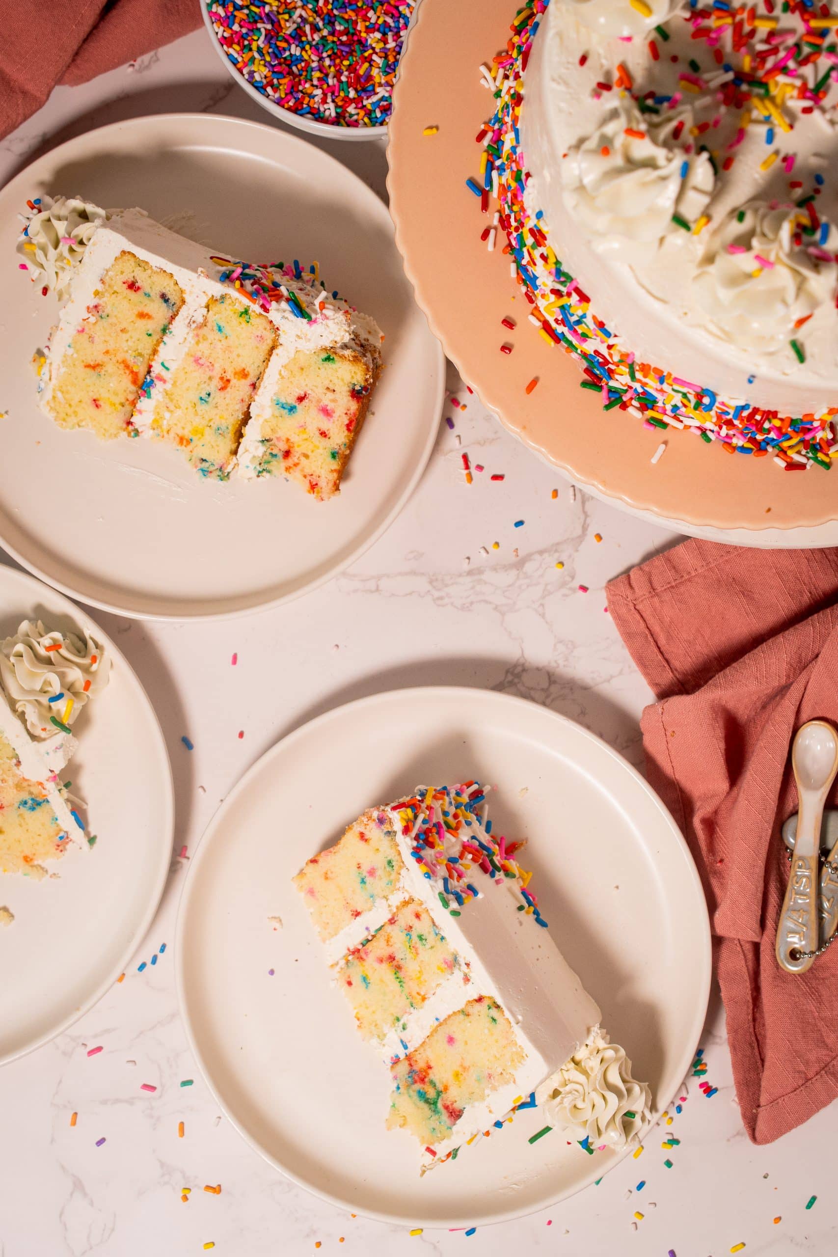 Overhead view of sliced Funfetti cake with sprinkles and vanilla buttercream frosting, displayed on white plates.
