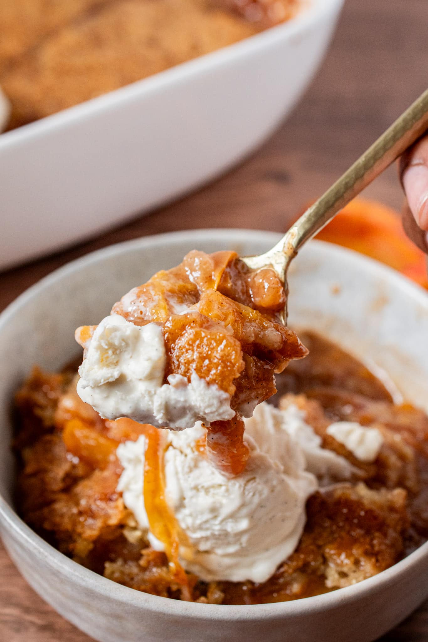 Close-up of a spoonful of warm peach cobbler and vanilla ice cream being lifted from a bowl