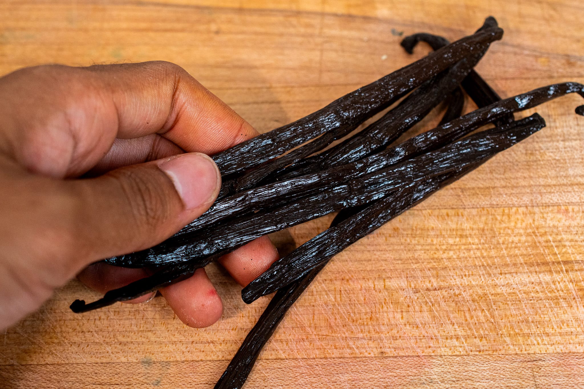 A bunch of vanilla beans on a wood cutting board ready to be used.