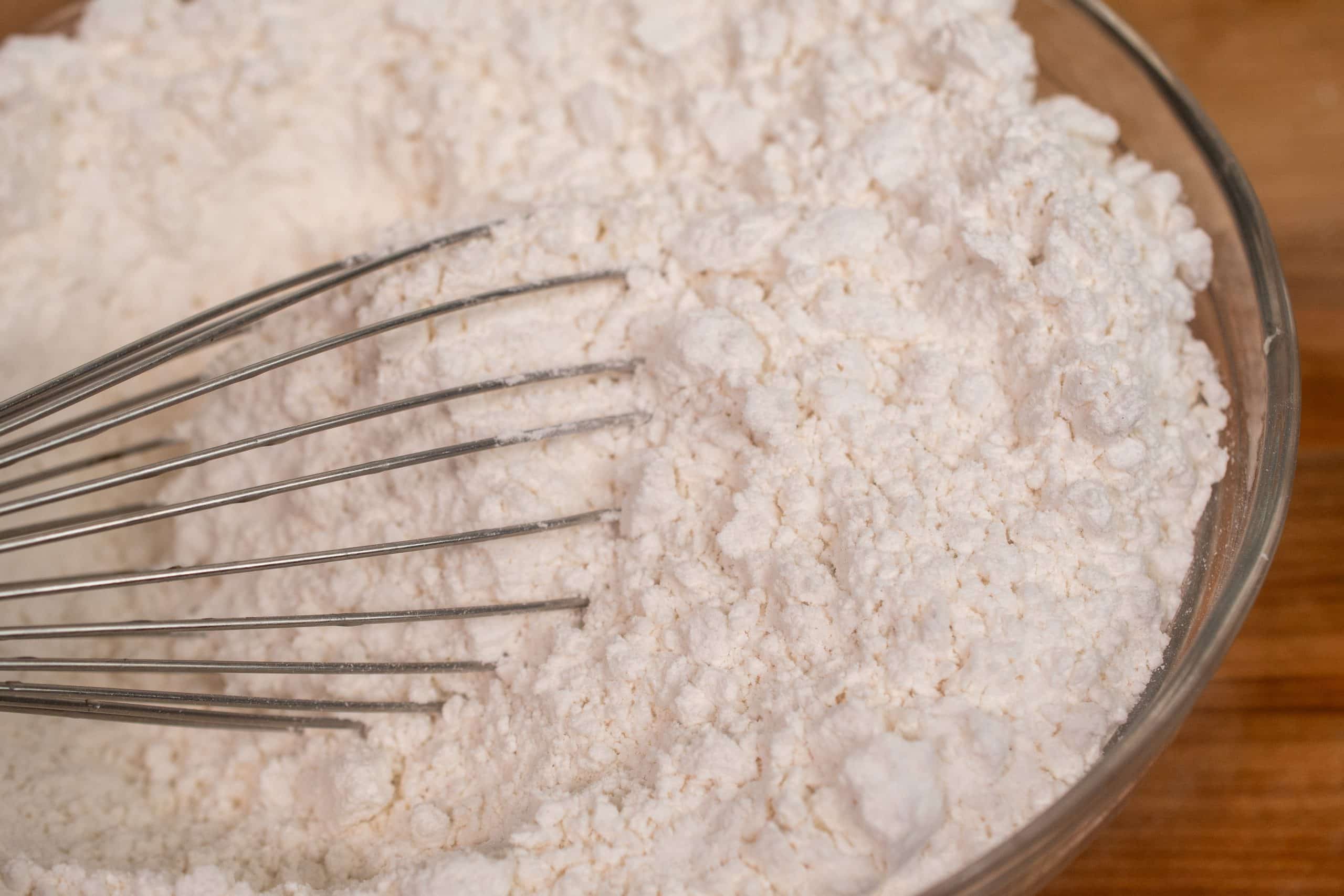 Mixing dry ingredients for Funfetti cupcakes, including flour, baking powder, and salt, with a whisk.