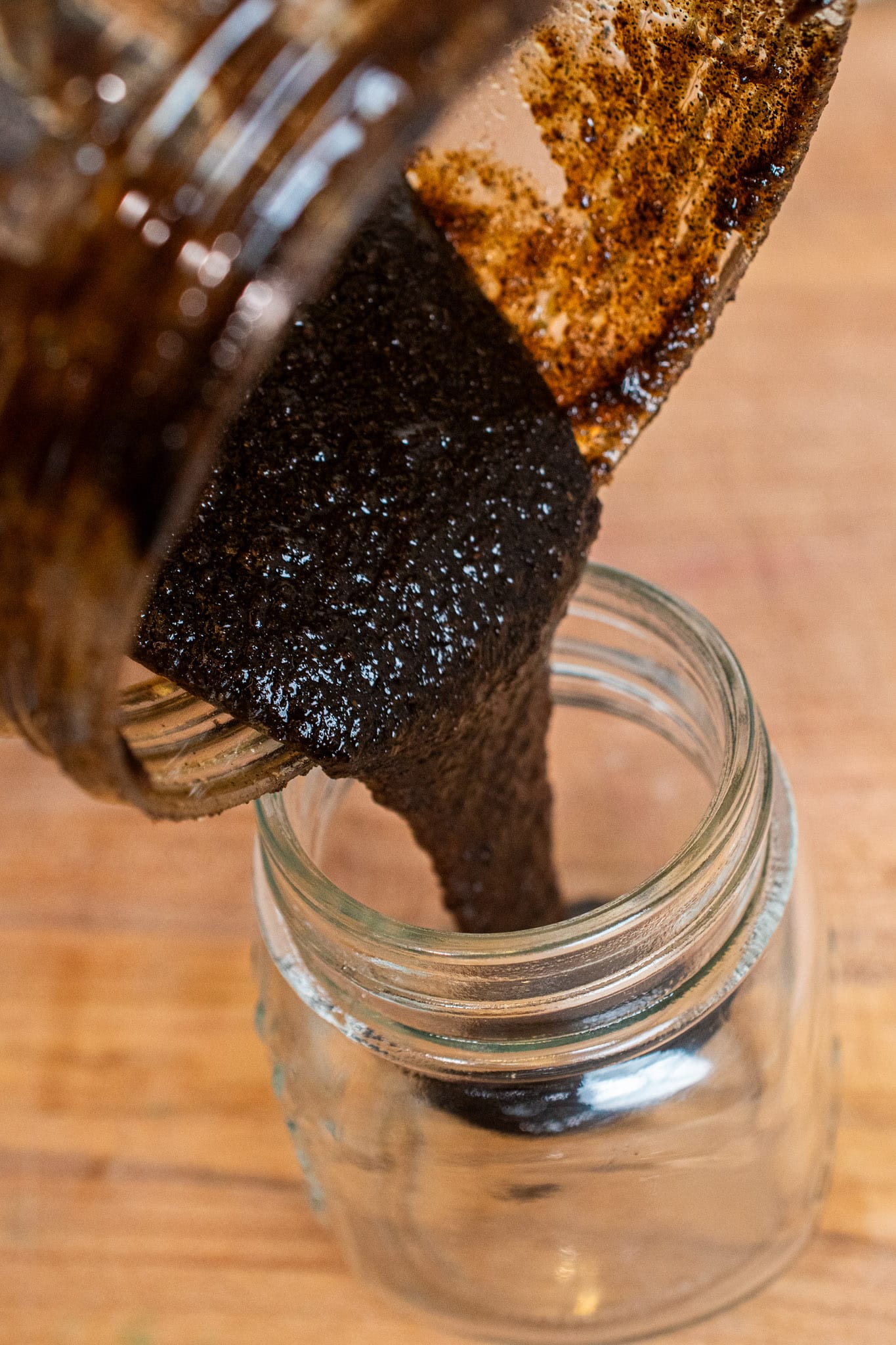 Pouring thick vanilla bean paste into a clean glass jar ready to be used.