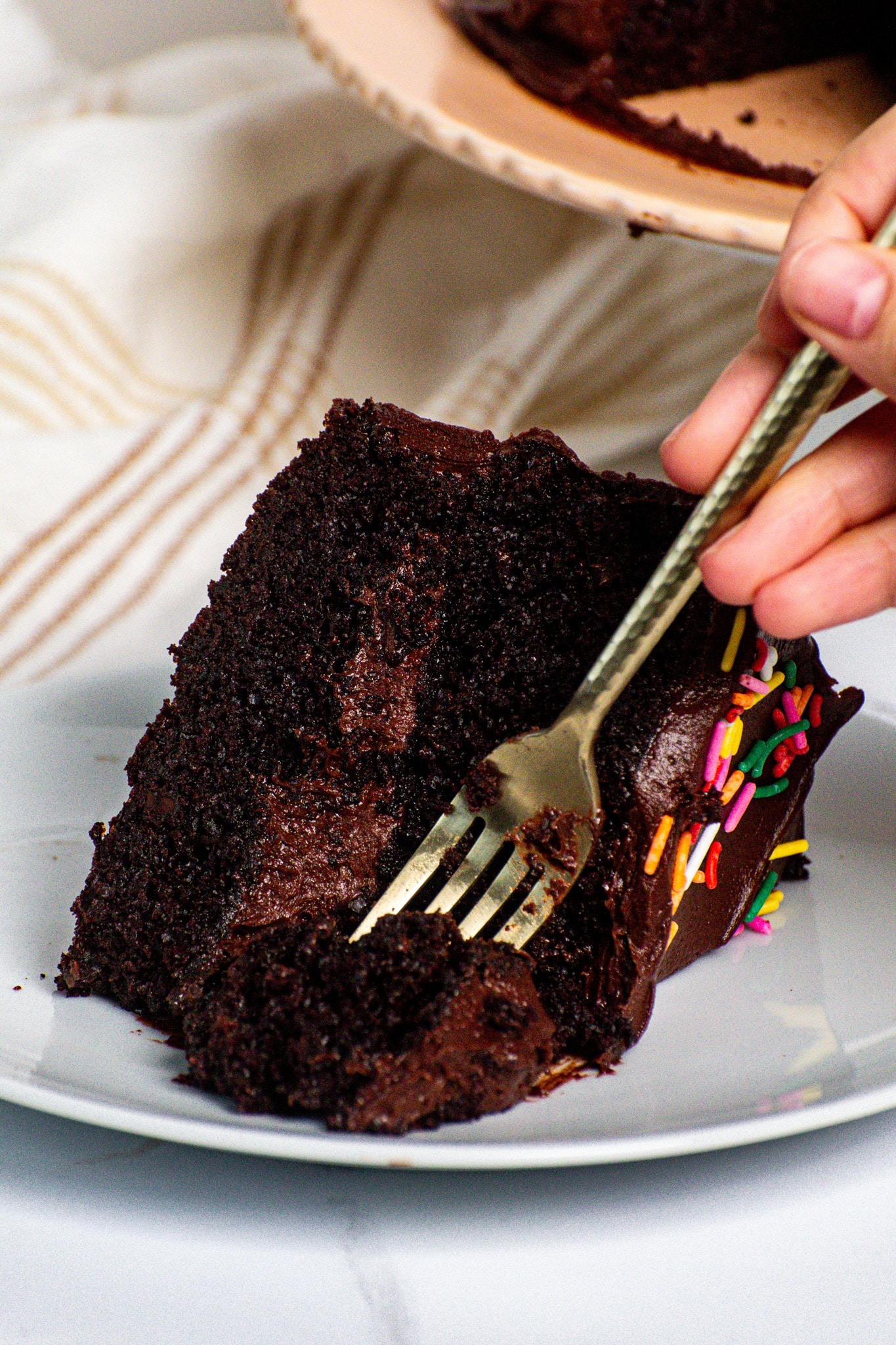 Fork cutting into a super moist chocolate cake slice with fudgy chocolate frosting