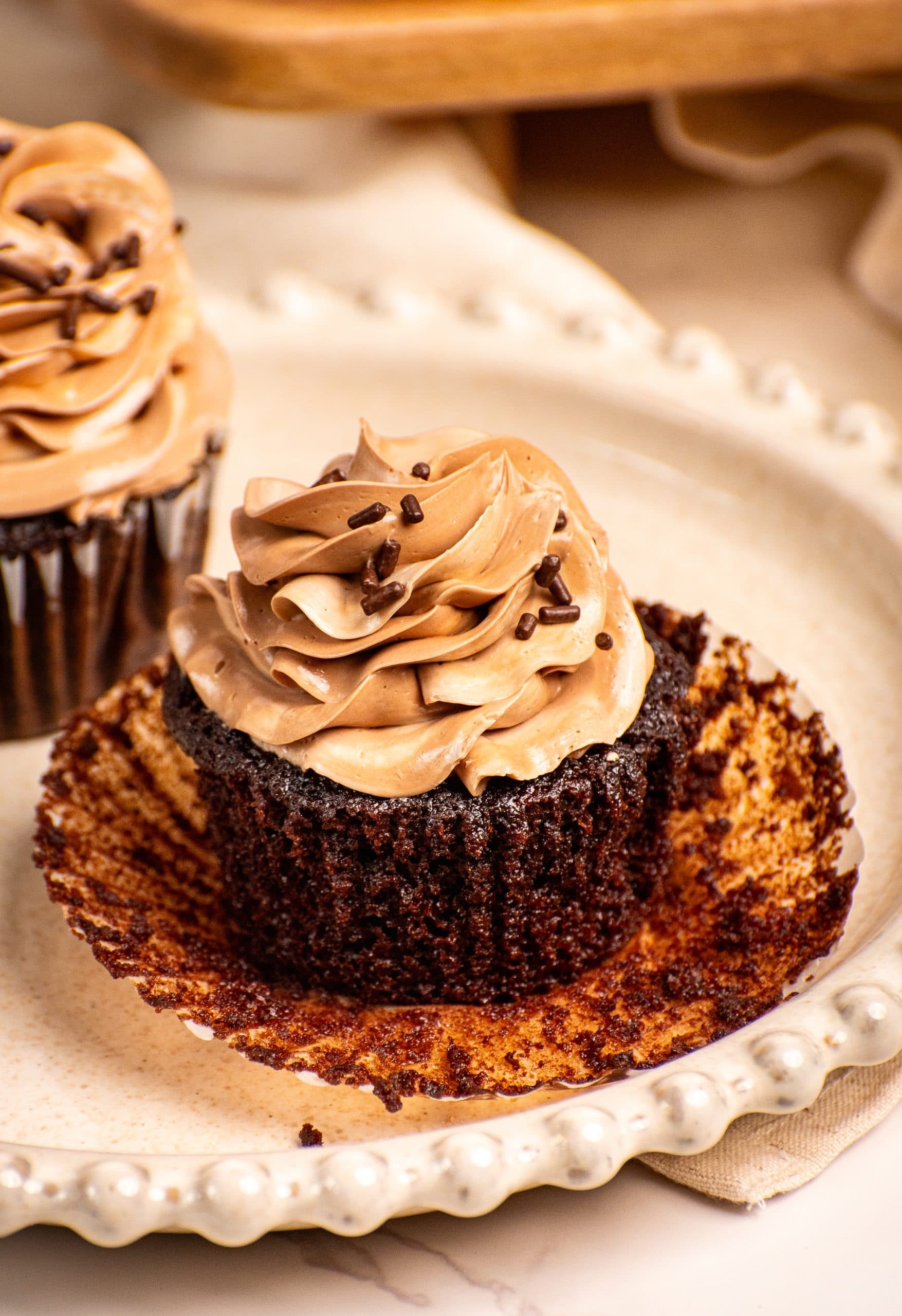 Moist chocolate cupcake with swirled chocolate frosting and chocolate sprinkles on a decorative plate.