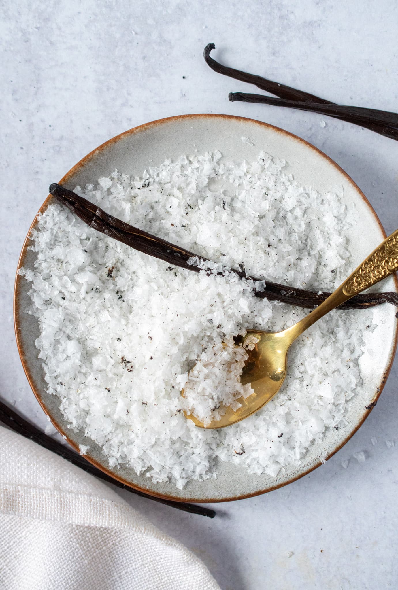 Homemade vanilla salt in a ceramic bowl with a gold spoon and vanilla beans.