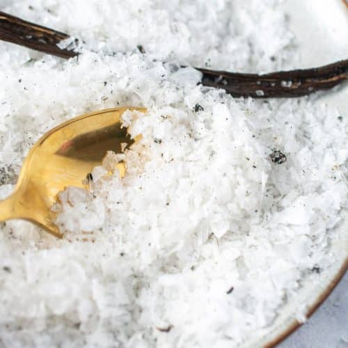 Close-up of gold spoon scooping flaky vanilla salt with vanilla bean