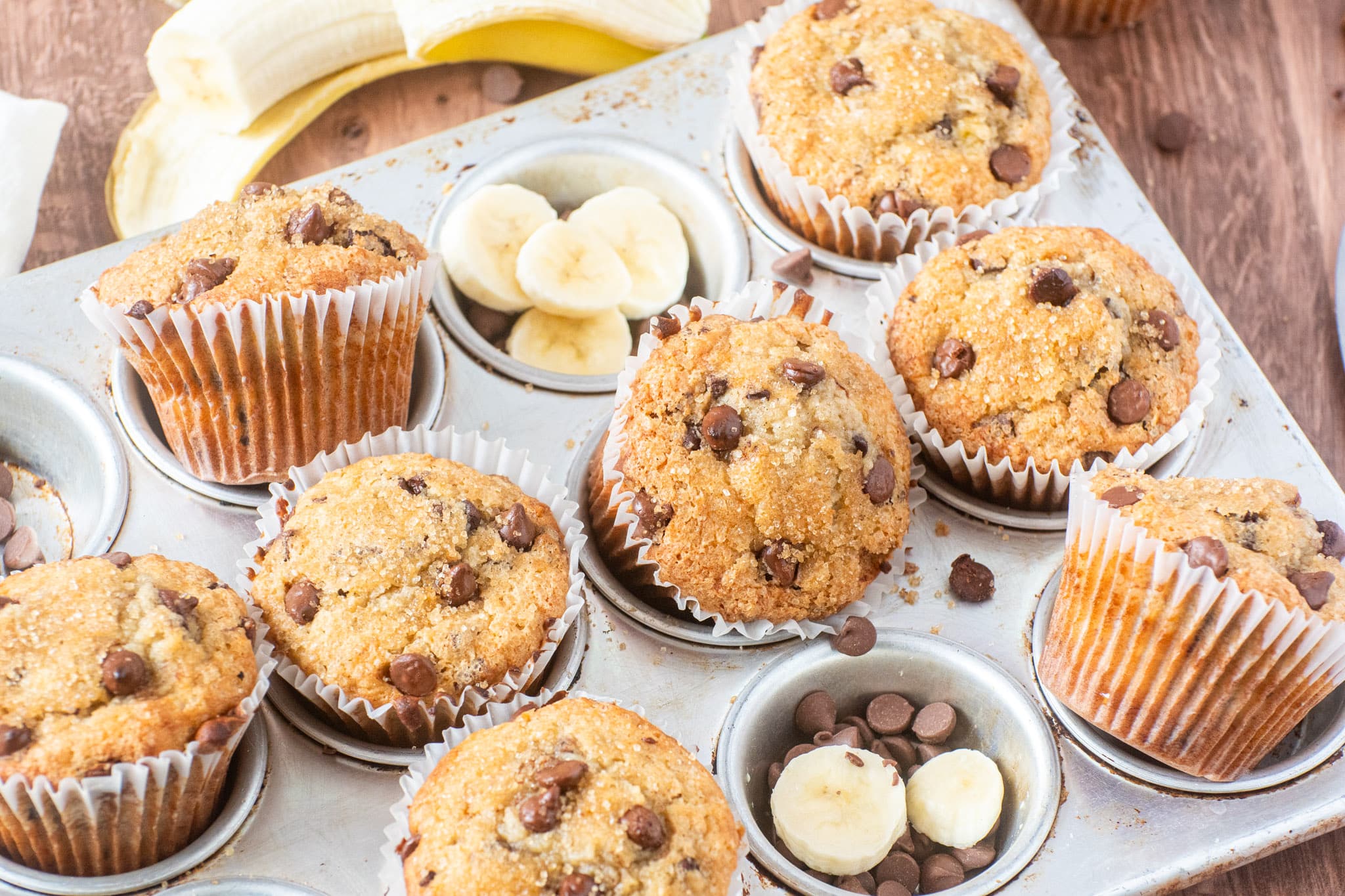 Bakery-style banana muffins with chocolate chips in a muffin tin, topped with a golden crumble