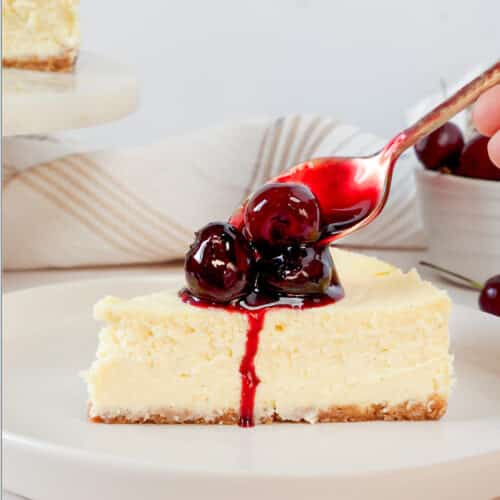 spooning homemade cherry compote over a slice of cherry cheesecake