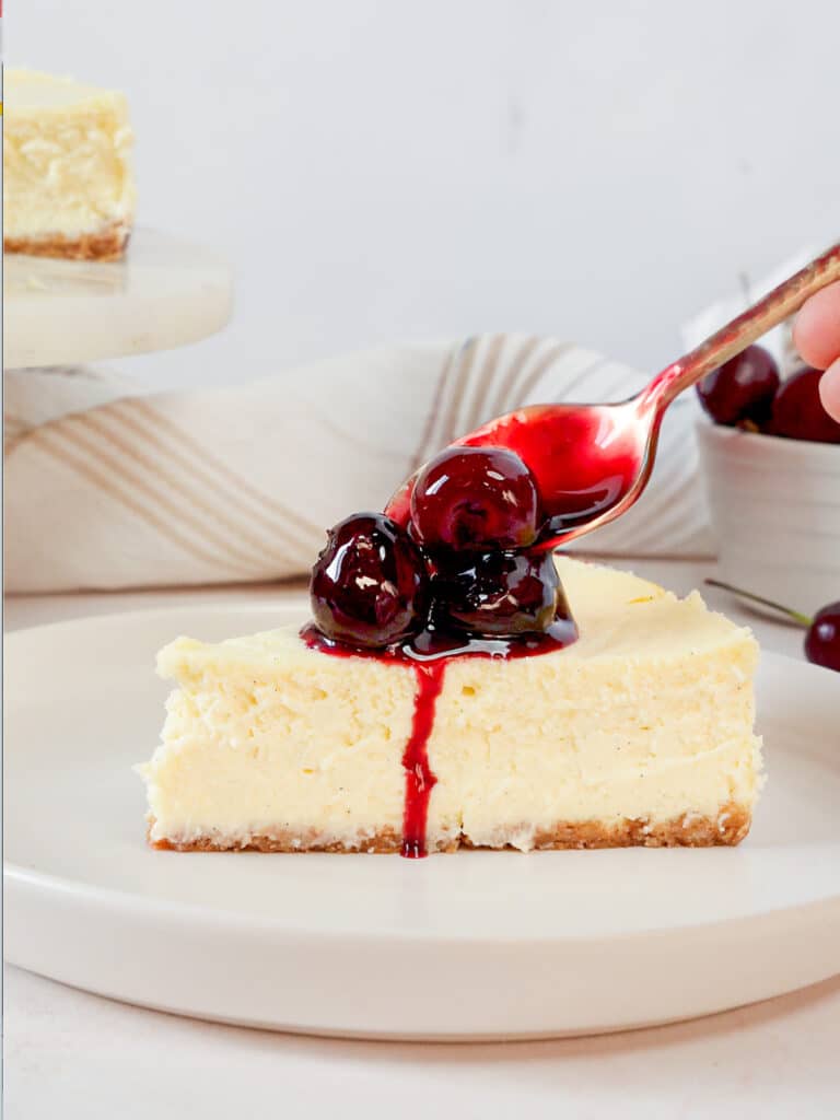 spooning homemade cherry compote over a slice of cherry cheesecake