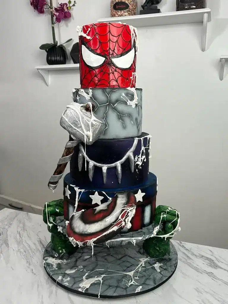 Multi-tiered superhero-themed cake with designs inspired by Captain America, Spider-Man, and Batman.