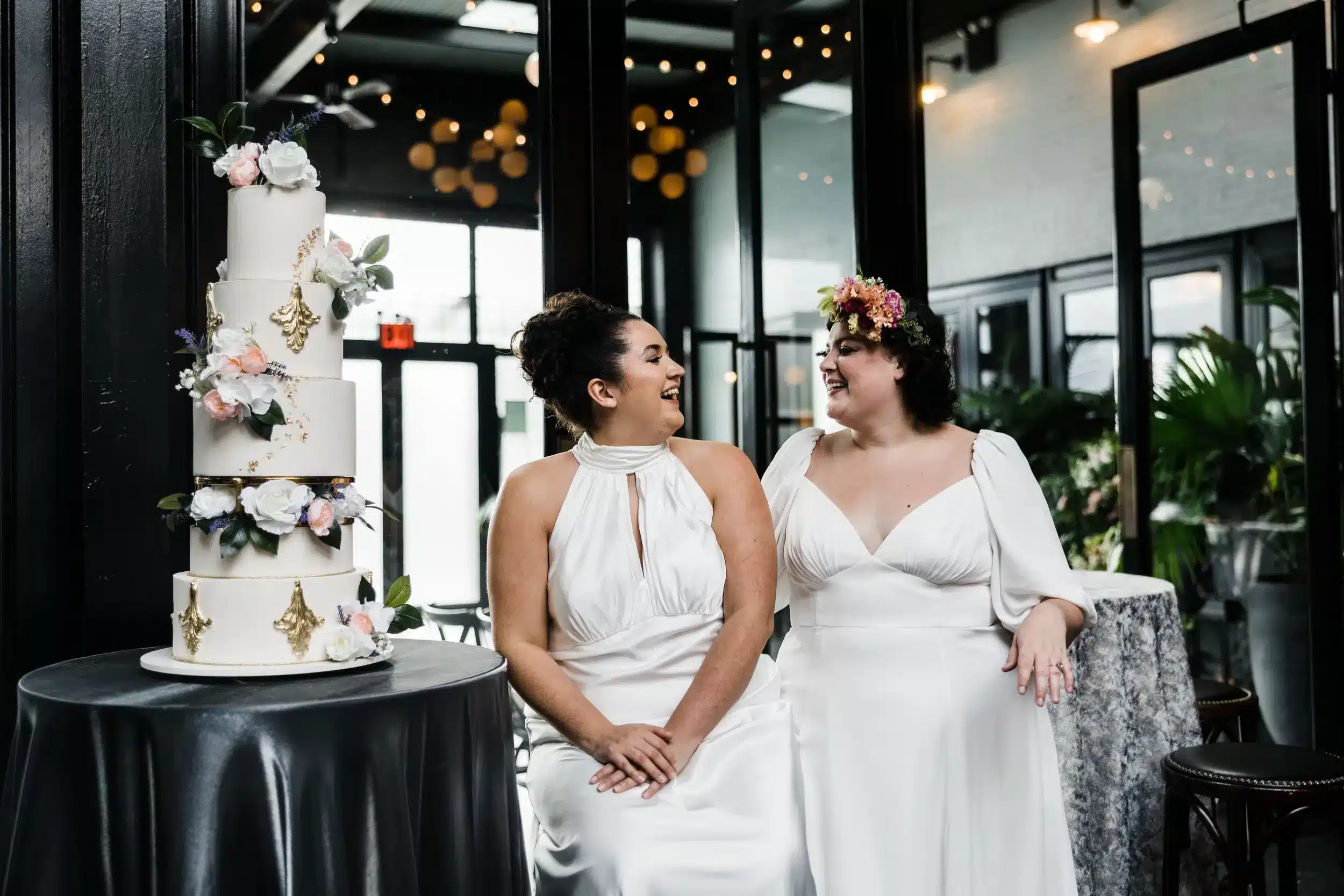 Elegant wedding cake with floral accents, captured alongside two brides during their wedding celebration.