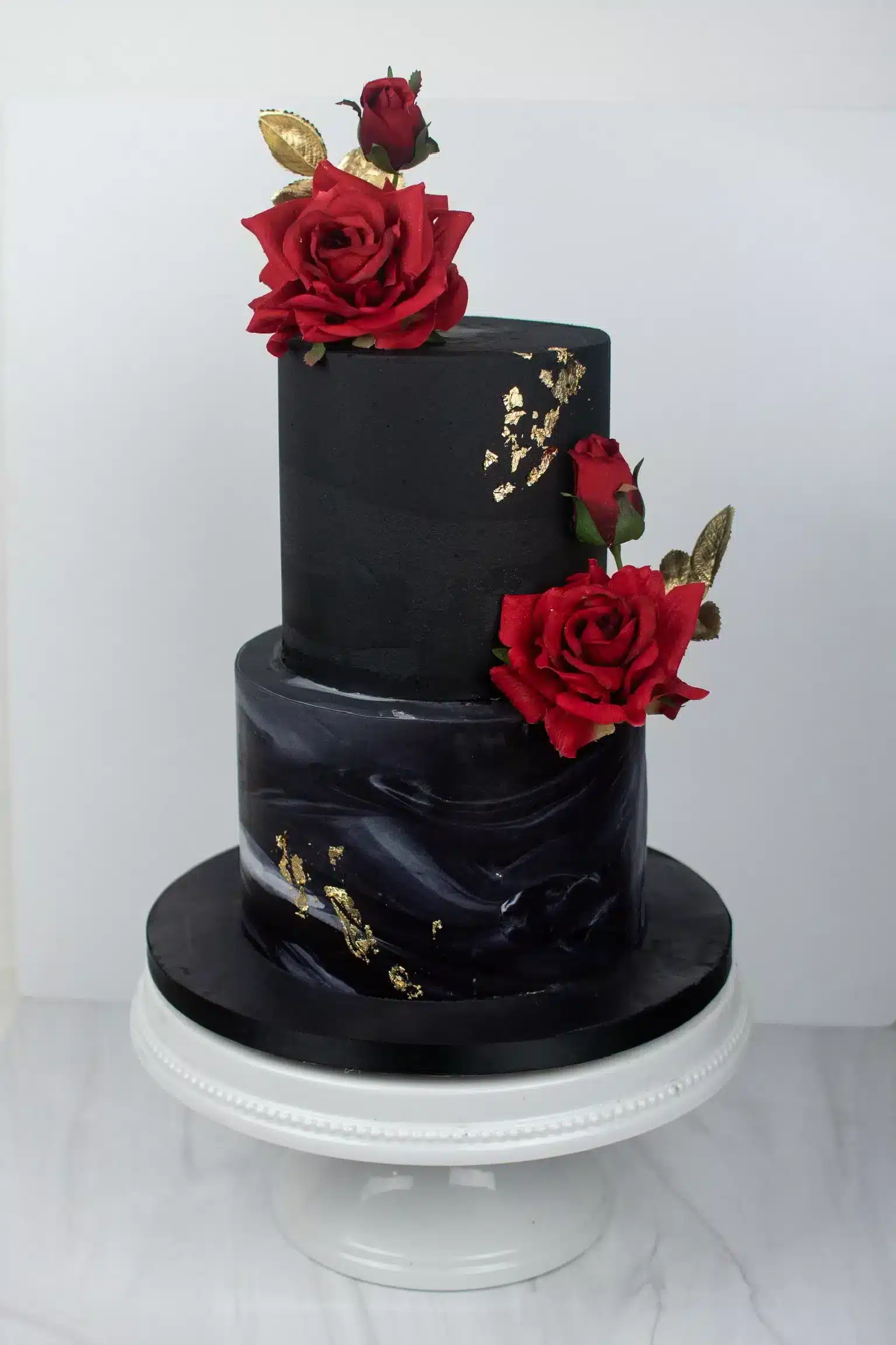 Black two-tier cake with red roses and gold accents, ideal for modern or gothic-themed celebrations.