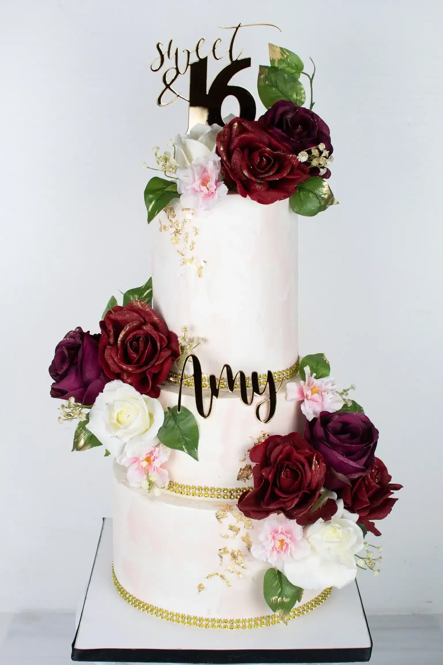 Wedding cake with burgundy and white flowers, complemented by gold accents, ideal for elegant weddings.
