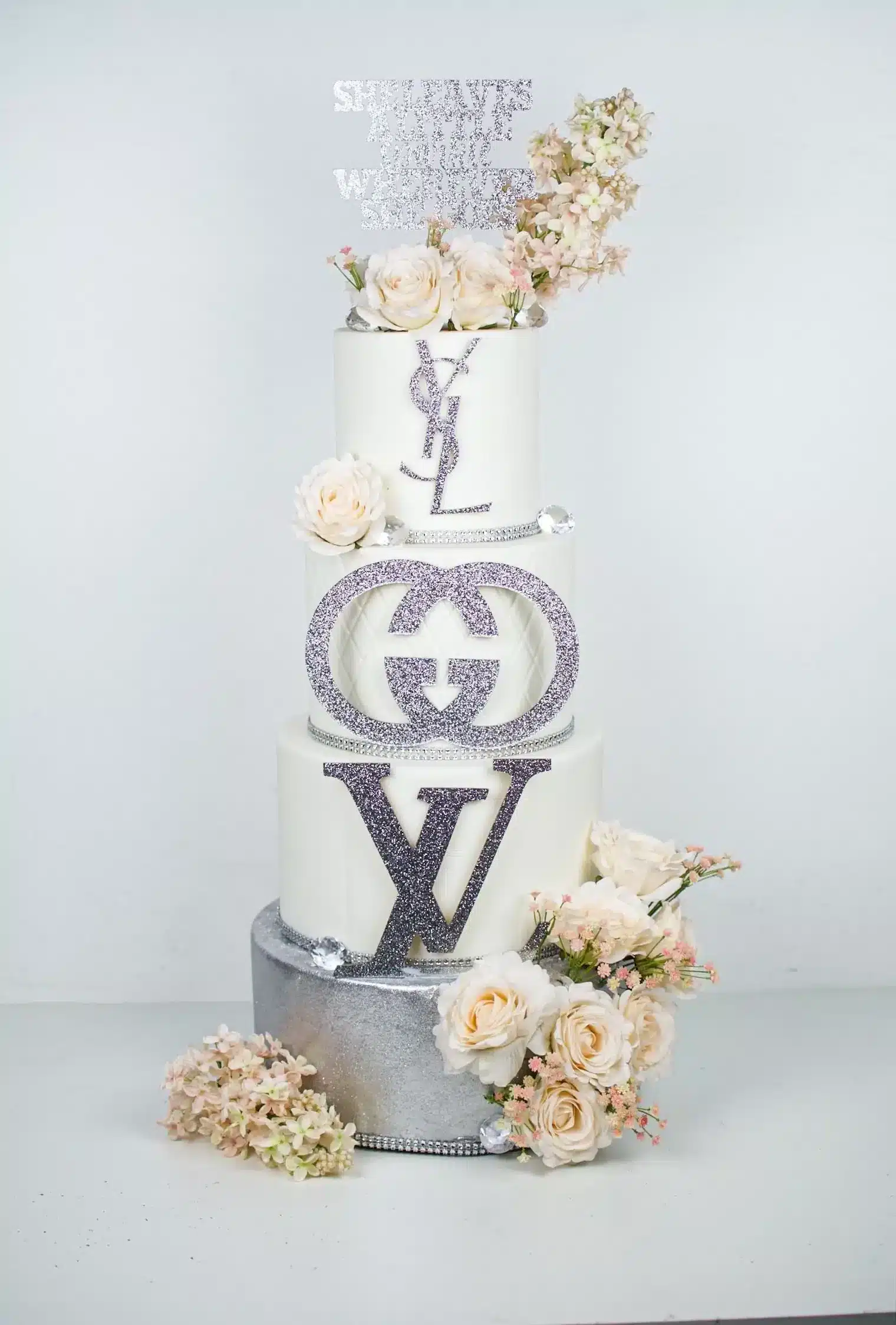 Luxury designer-themed cake featuring Louis Vuitton, Gucci, and Yves Saint Laurent logos with white and blush flowers.