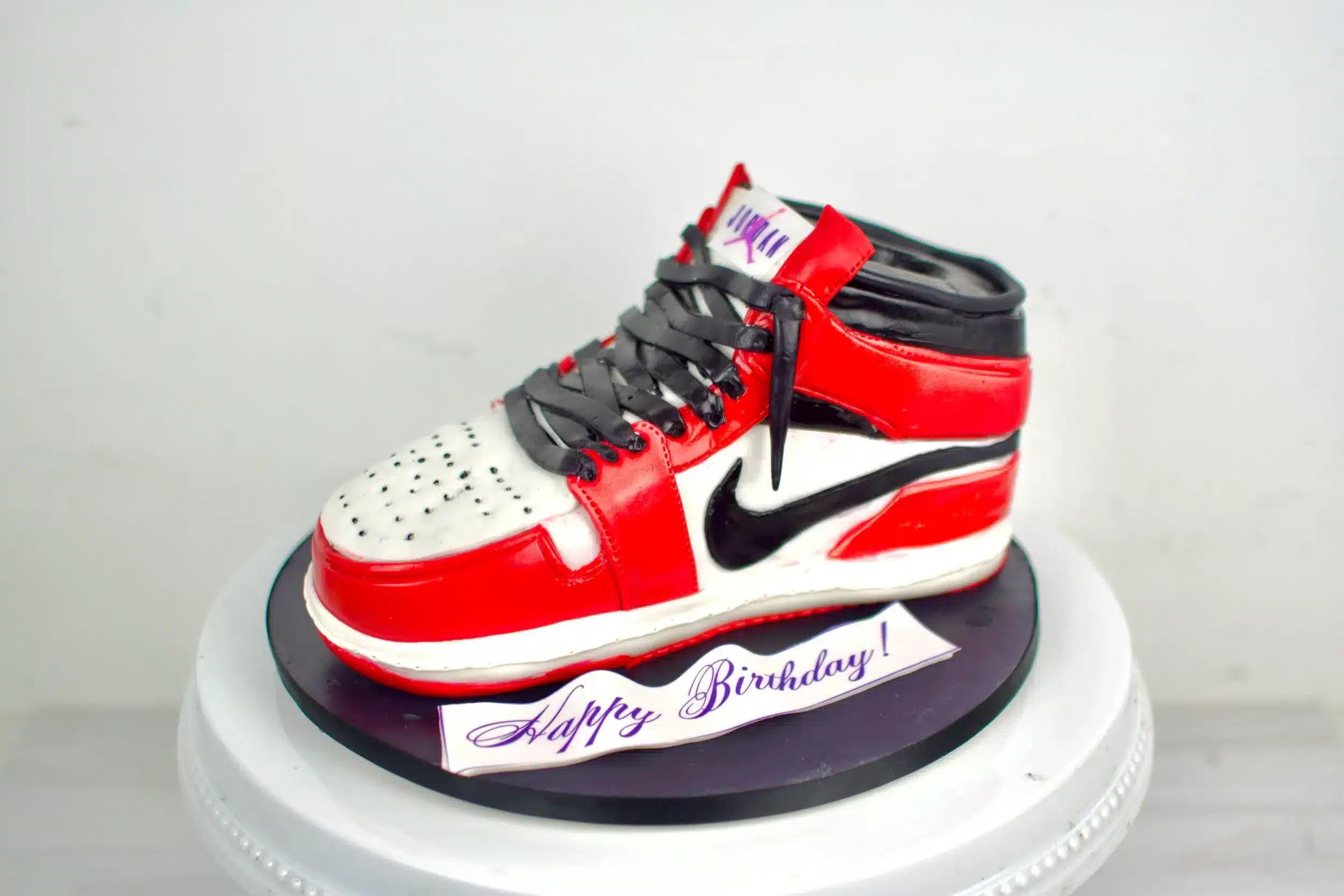 Air Jordan sneaker cake in red, white, and black with realistic fondant details, ideal for sneaker lovers or birthday celebrations.