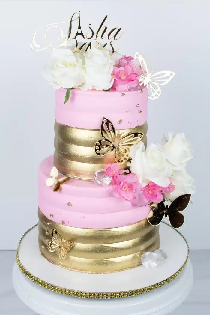 Two-tier pink and gold cake with fresh flowers, perfect for birthdays, anniversaries, or elegant celebrations.