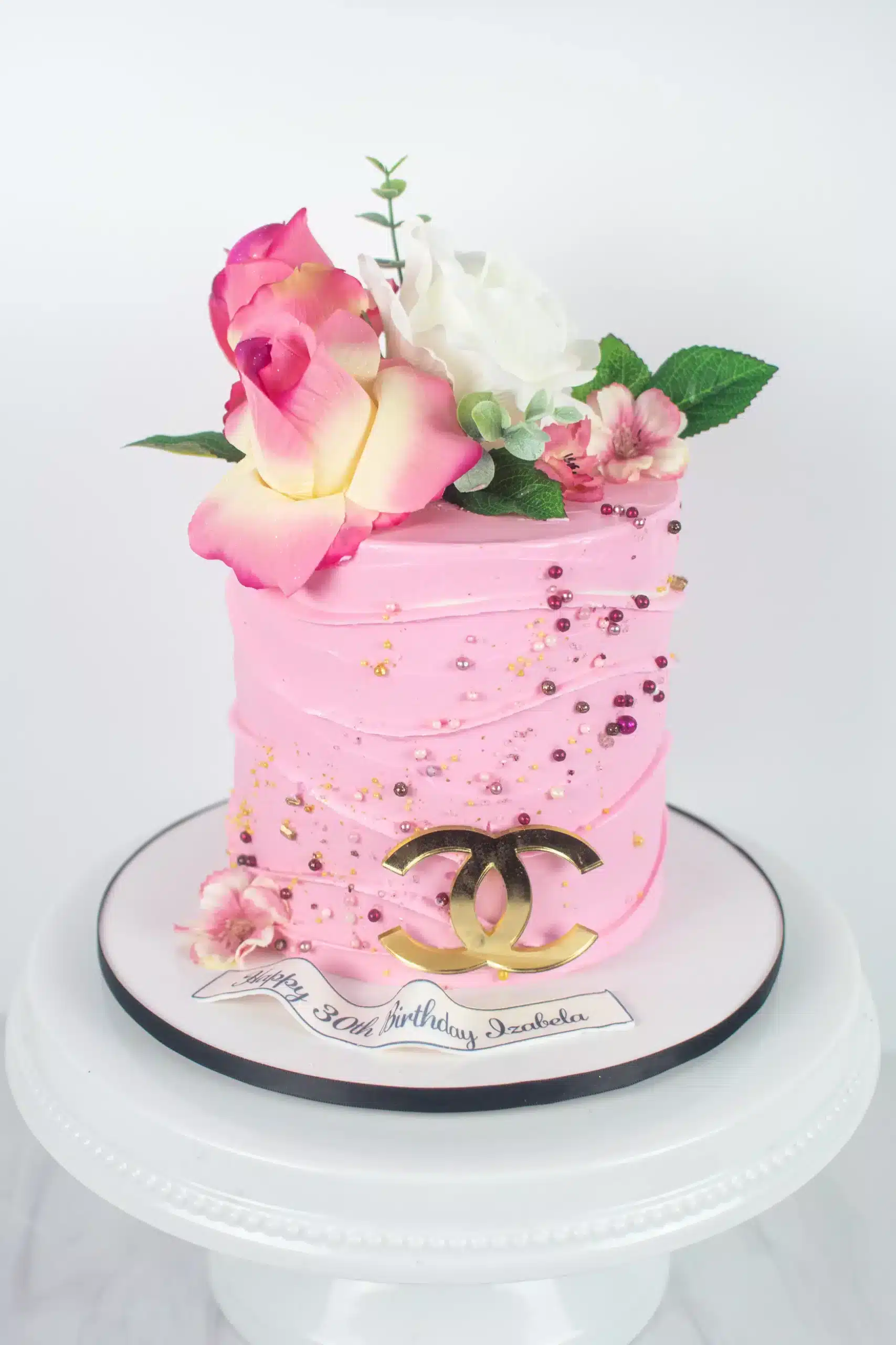 Pink single-tier cake with fresh flowers and green leaves, ideal for birthdays or spring-themed celebrations.