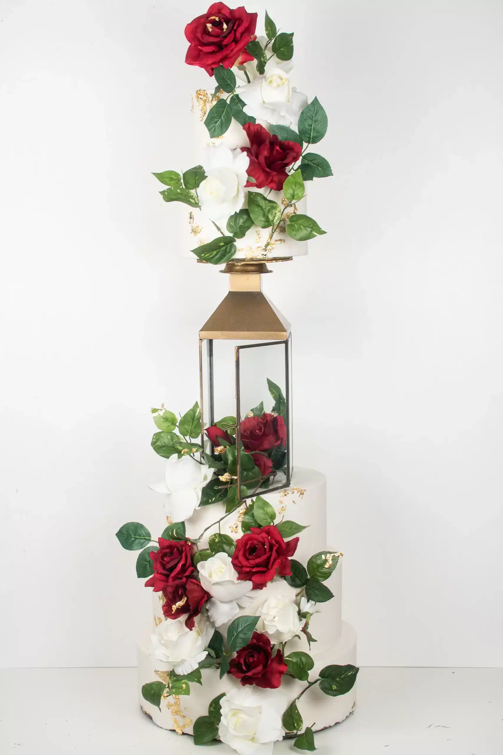 Three-tier wedding cake with red and white roses and gold geometric accents, ideal for romantic or formal weddings.