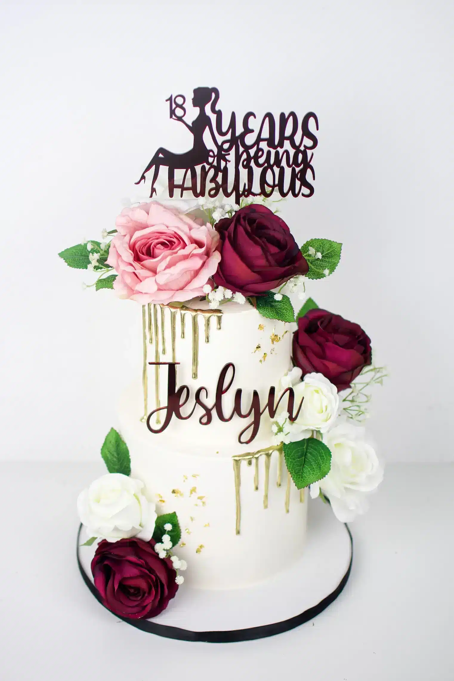 Two-tier birthday cake with fresh flowers, gold accents, and a personalized topper, ideal for elegant birthday celebrations.