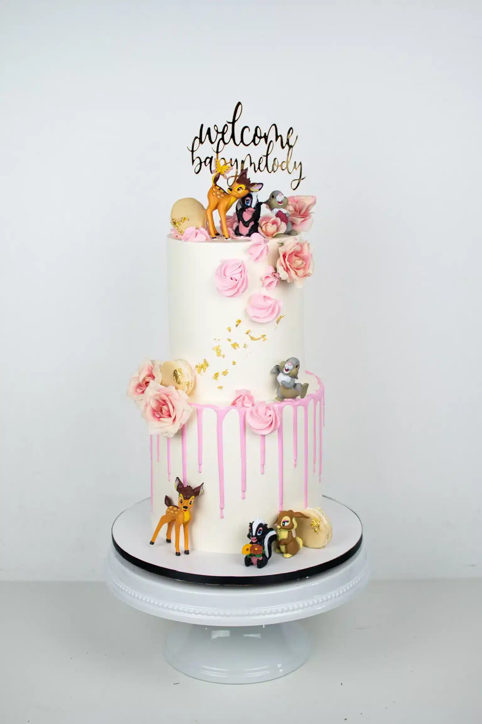 Pink two-tier cake with fresh flowers, gold leaf accents, and fondant butterflies, ideal for spring-themed celebrations or birthdays.