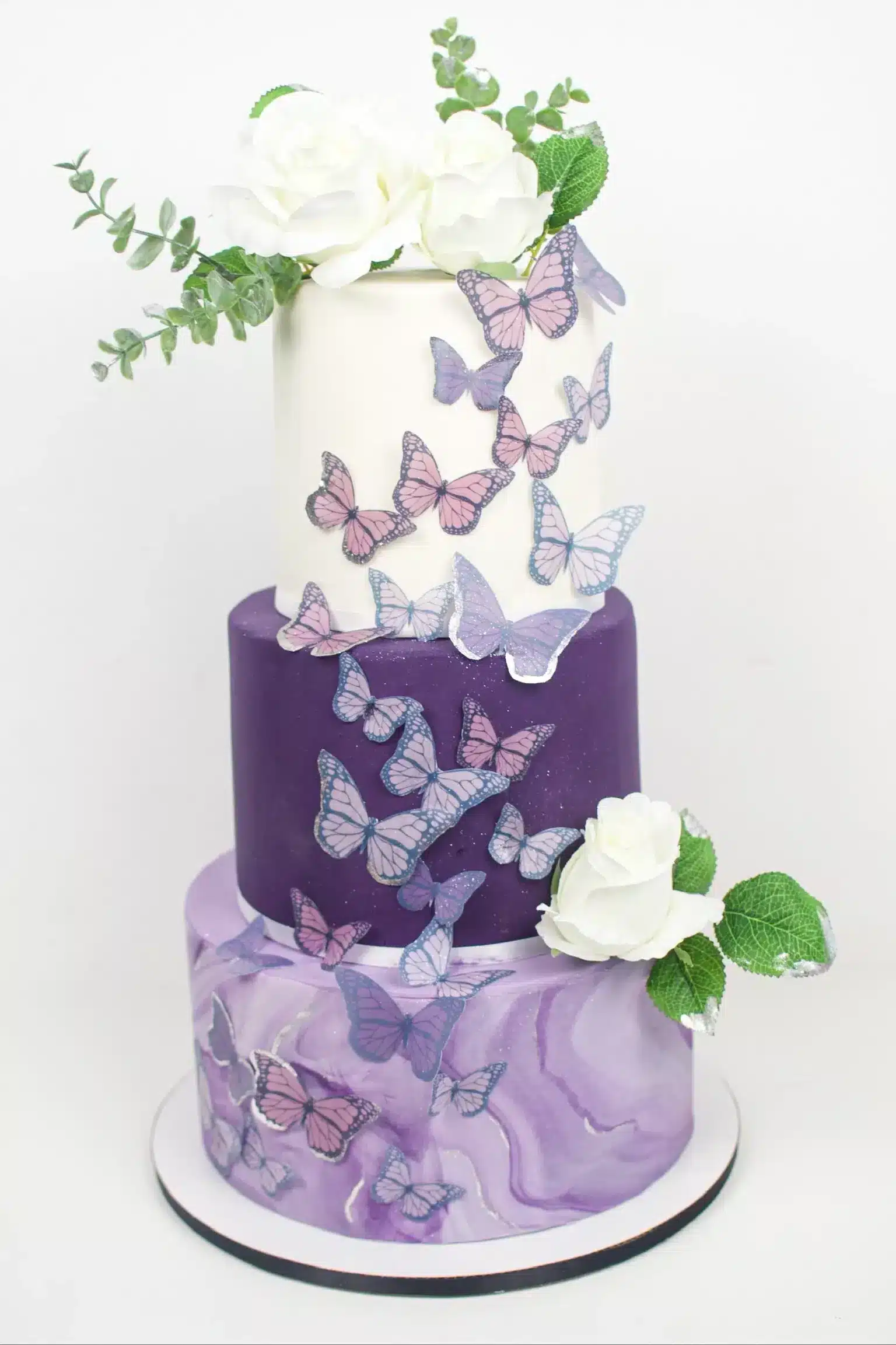 Two-tier purple cake with cascading white flowers and butterfly decorations, perfect for weddings or special events.
