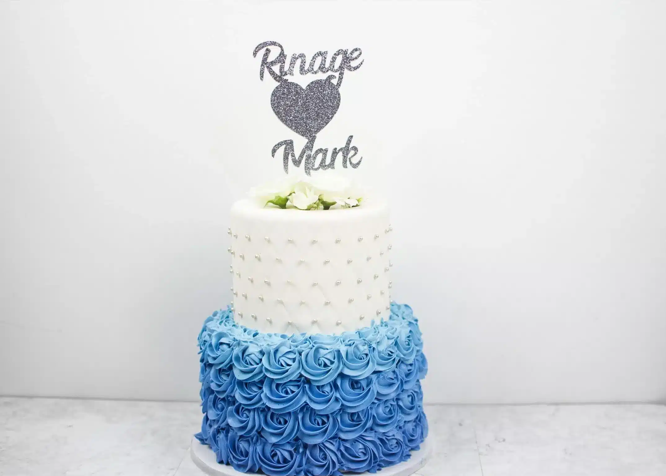 Two-tiered blue ombré buttercream cake with ruffled texture and wedding topper, perfect for weddings or anniversaries