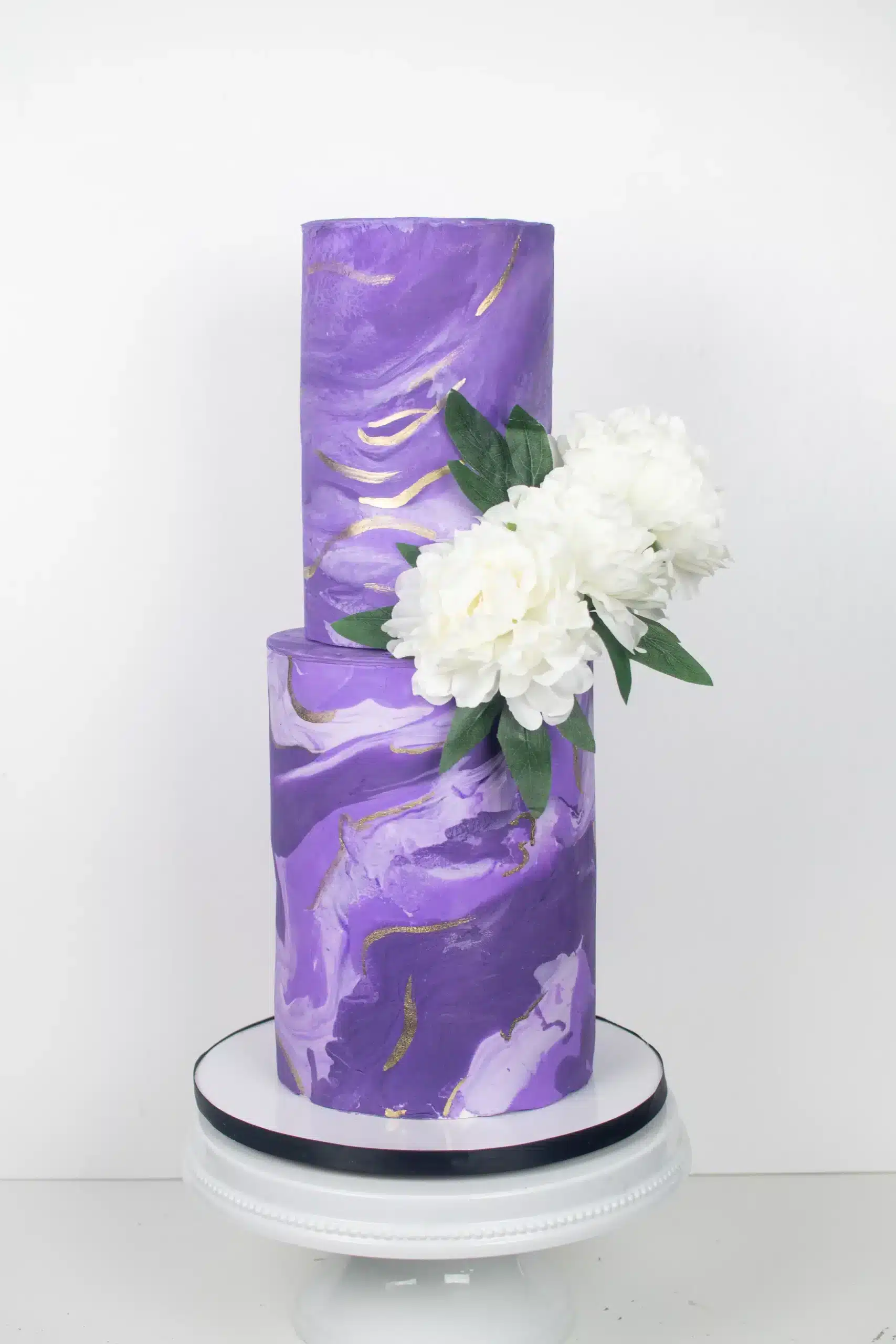 Two-tier purple buttercream cake with white flower decoration, ideal for weddings or milestone celebrations.