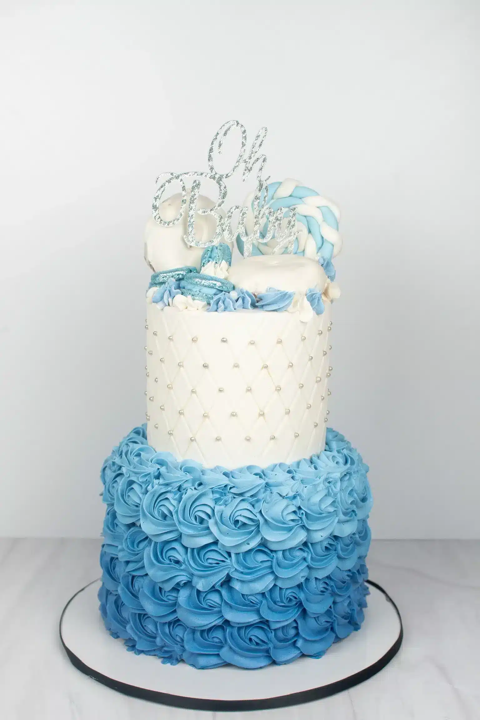 Blue and white two-tier cake with silver accents and blue flower decorations, perfect for weddings or baby showers.
