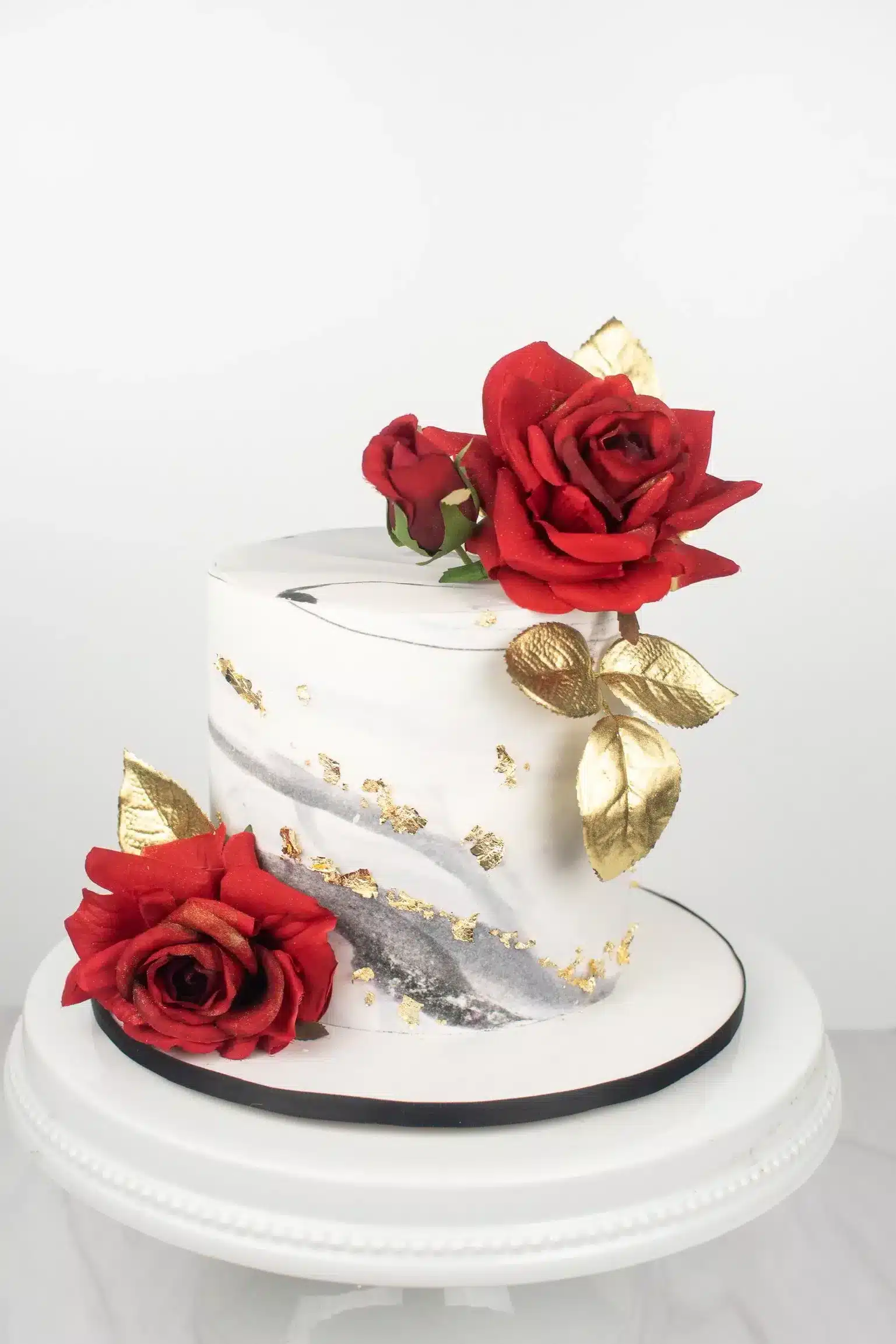 White buttercream cake with red roses and gold accents, ideal for weddings or special occasions.