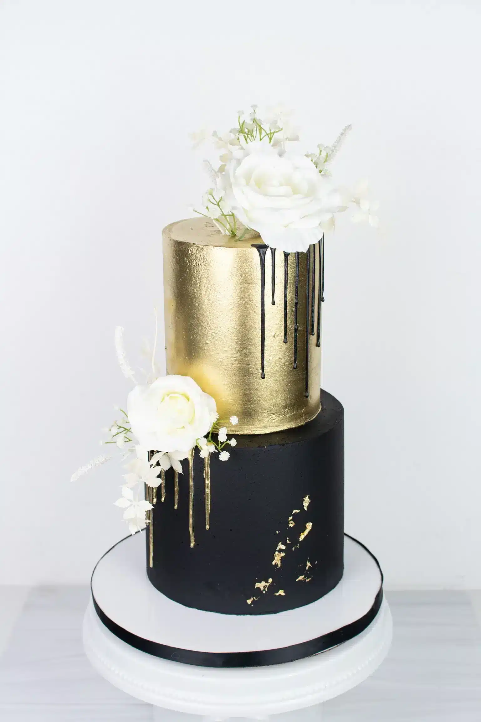 Black and gold buttercream cake with fresh flowers for elegant events.